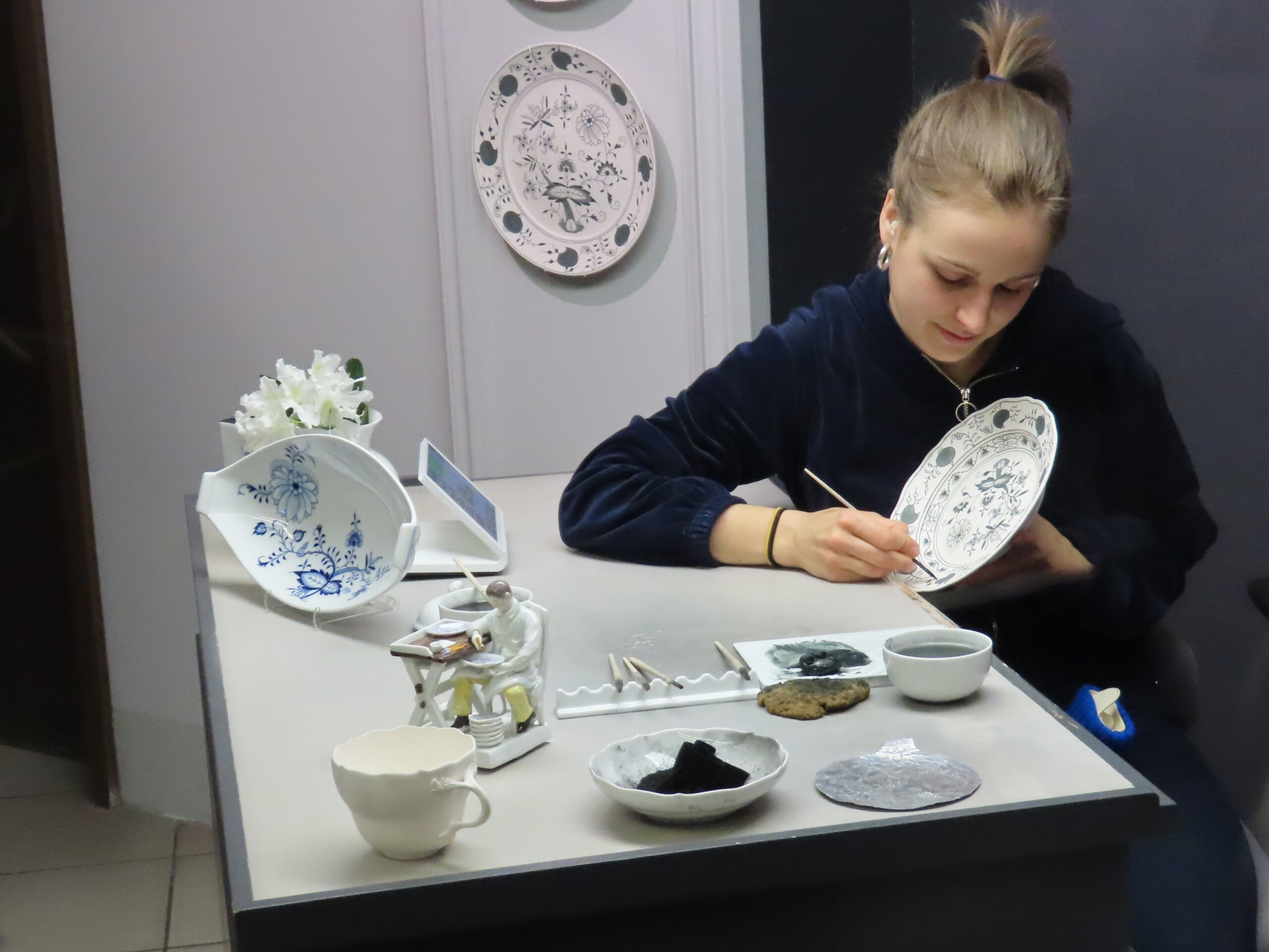 2024-04-24 Meissen - painting blue plate (also movie) Meissen porcelain is produced by hand. The paint the lady is using looks gray.